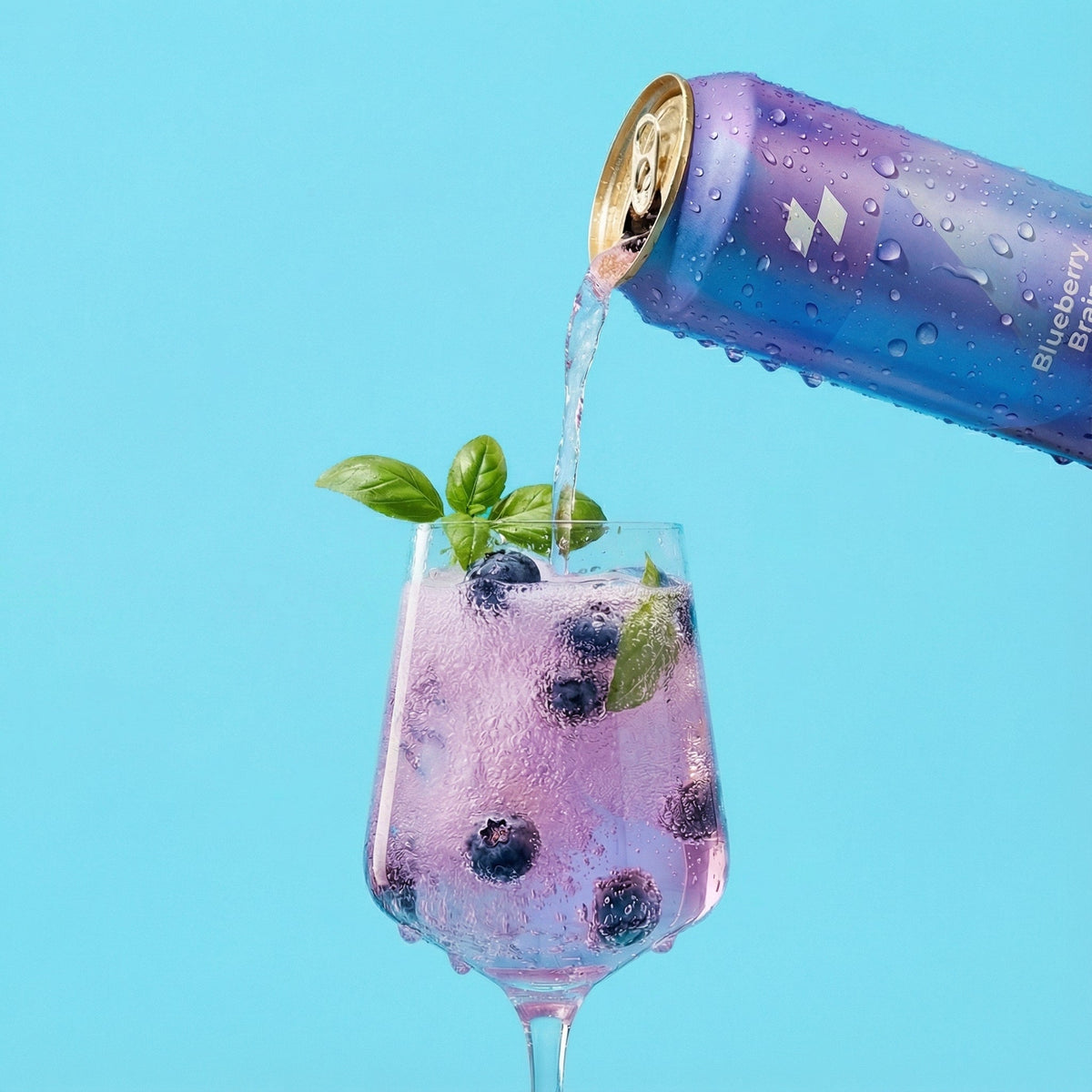 Blueberry-bramble can being poured into a glass with blueberries and mint leaves on a blue background