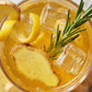 Glass of iced tea with lemon slices, ginger pieces, and a sprig of rosemary.