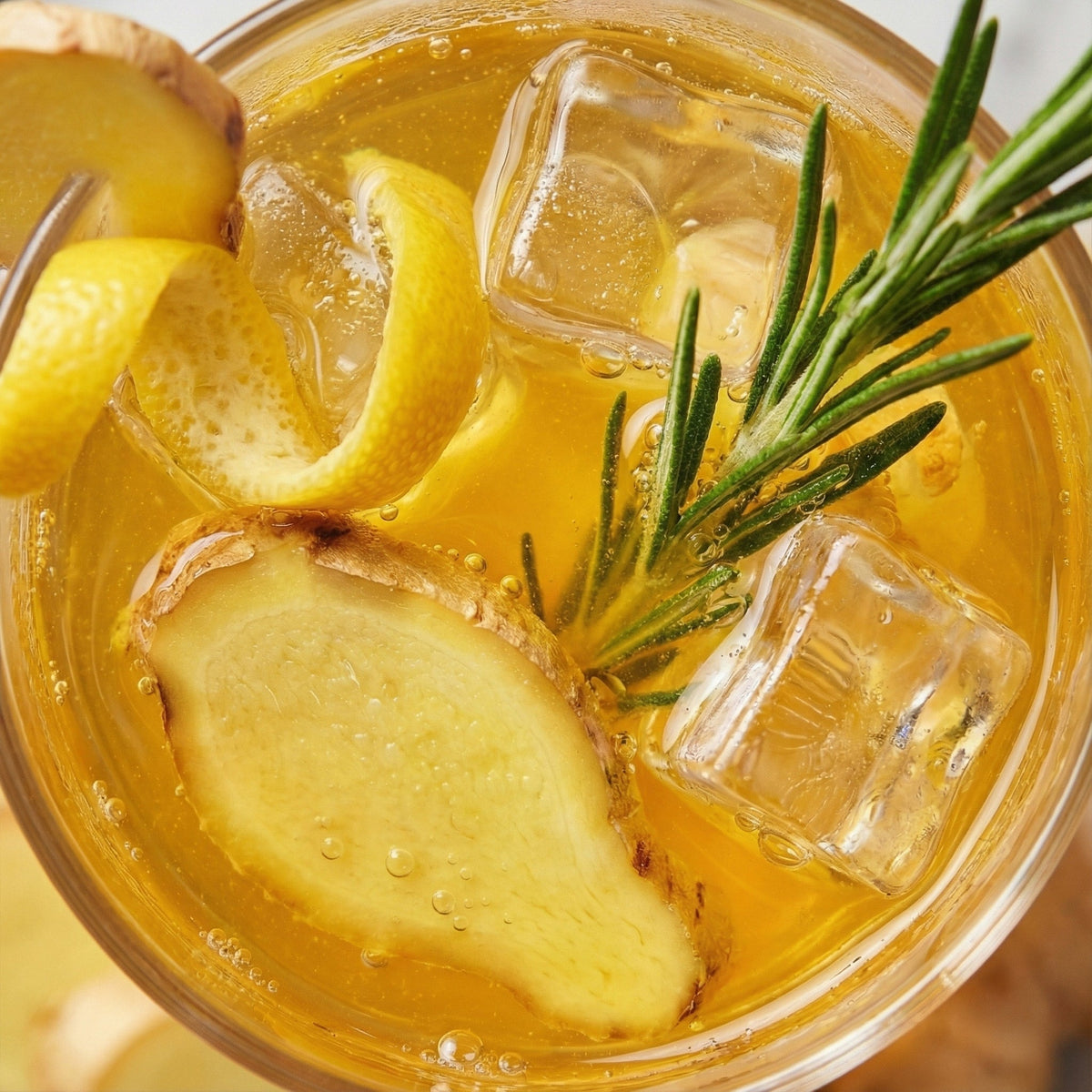 Glass of iced tea with lemon slices, ginger pieces, and a sprig of rosemary.