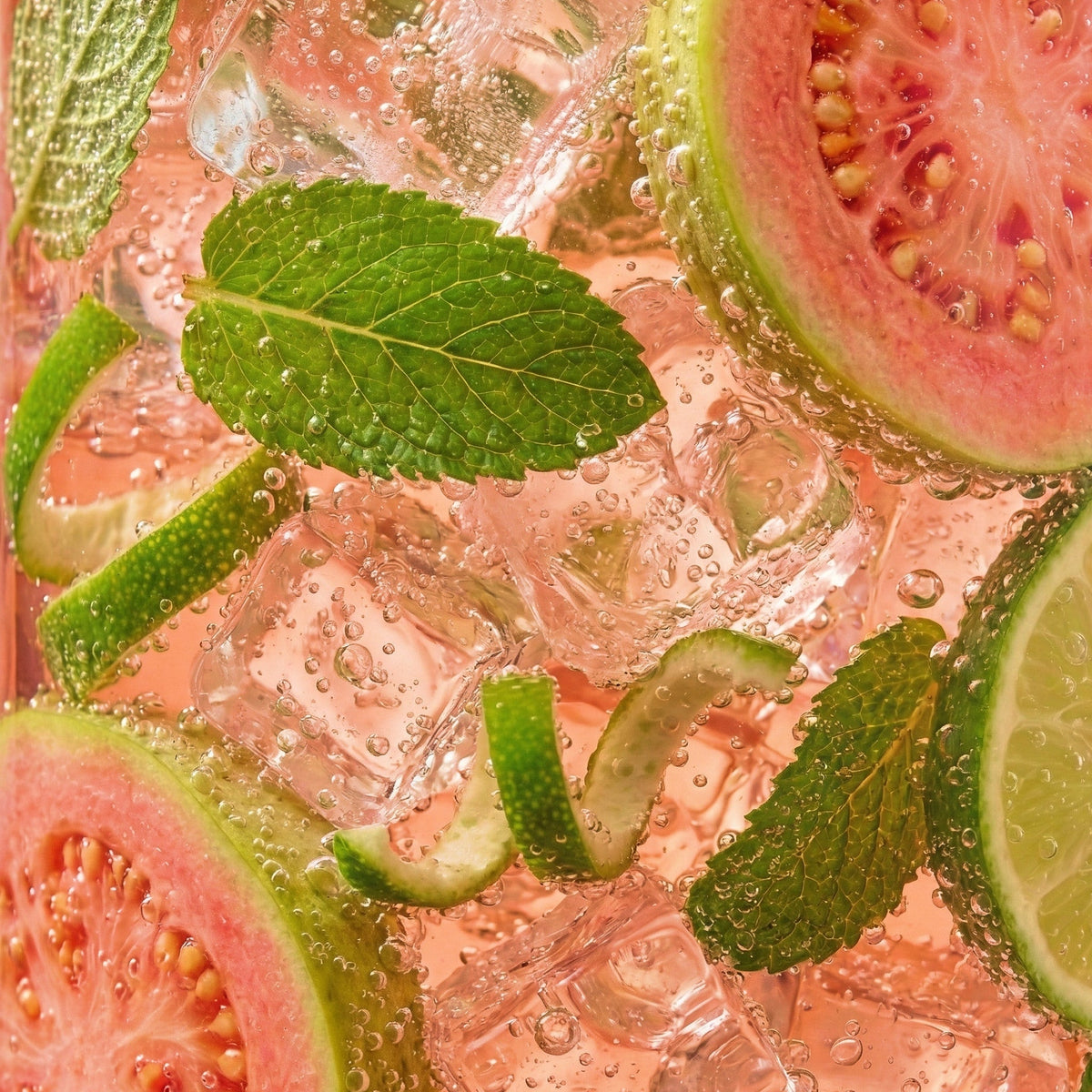 Sliced guava, lime, and mint leaves in a pink drink with ice cubes.